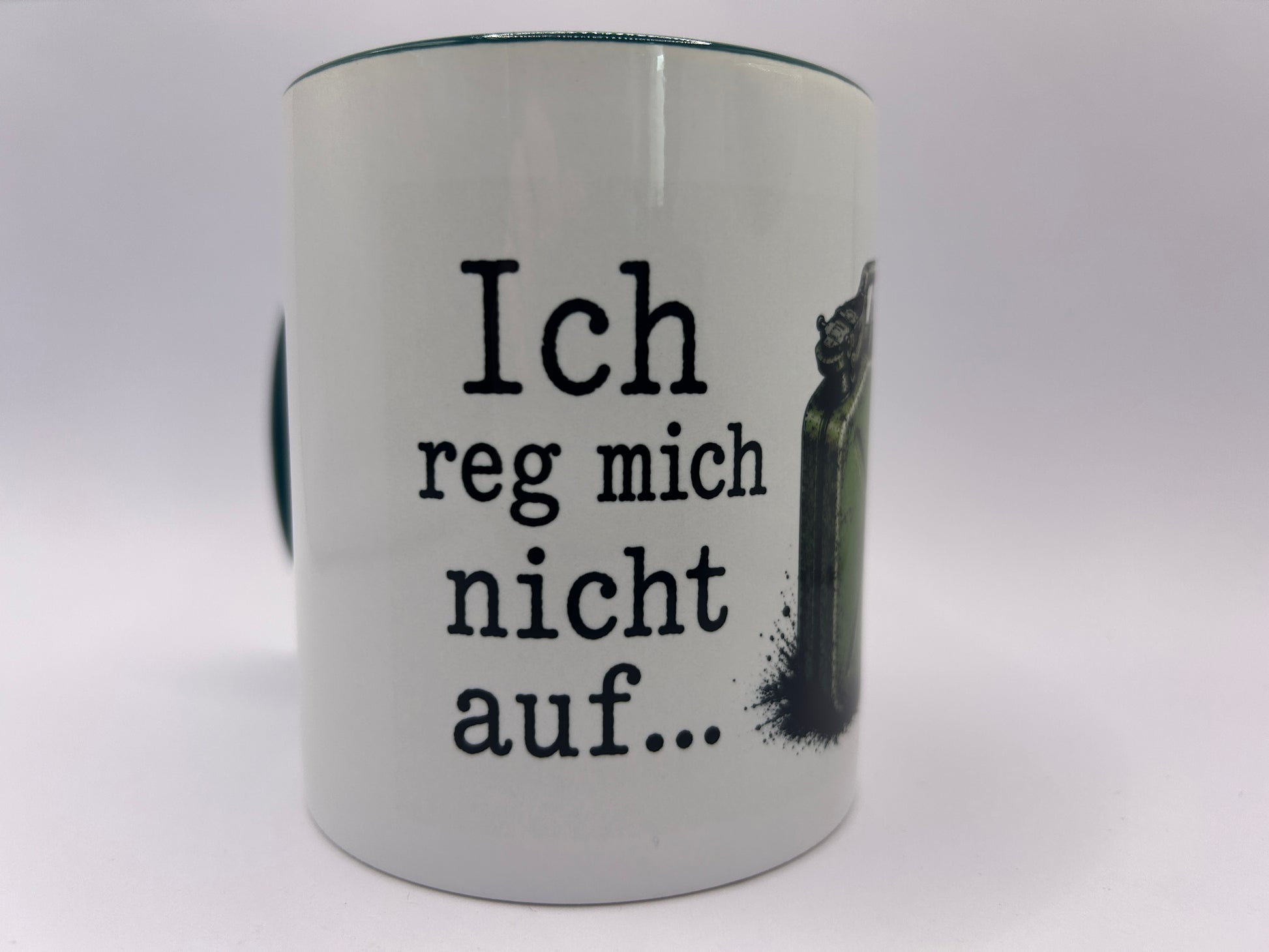 Nahaufnahme einer weißen Keramiktasse mit dem humorvollen Spruch „Ich reg mich nicht auf…“ in schwarzer Schrift. Rechts daneben ist ein Teil des Kanister-Motivs sichtbar.