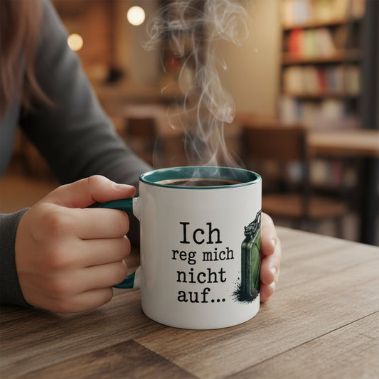 Nahaufnahme einer weißen Keramiktasse mit dem humorvollen Spruch „Ich reg mich nicht auf…“ in schwarzer Schrift. Rechts daneben ist ein Teil des Kanister-Motivs sichtbar.