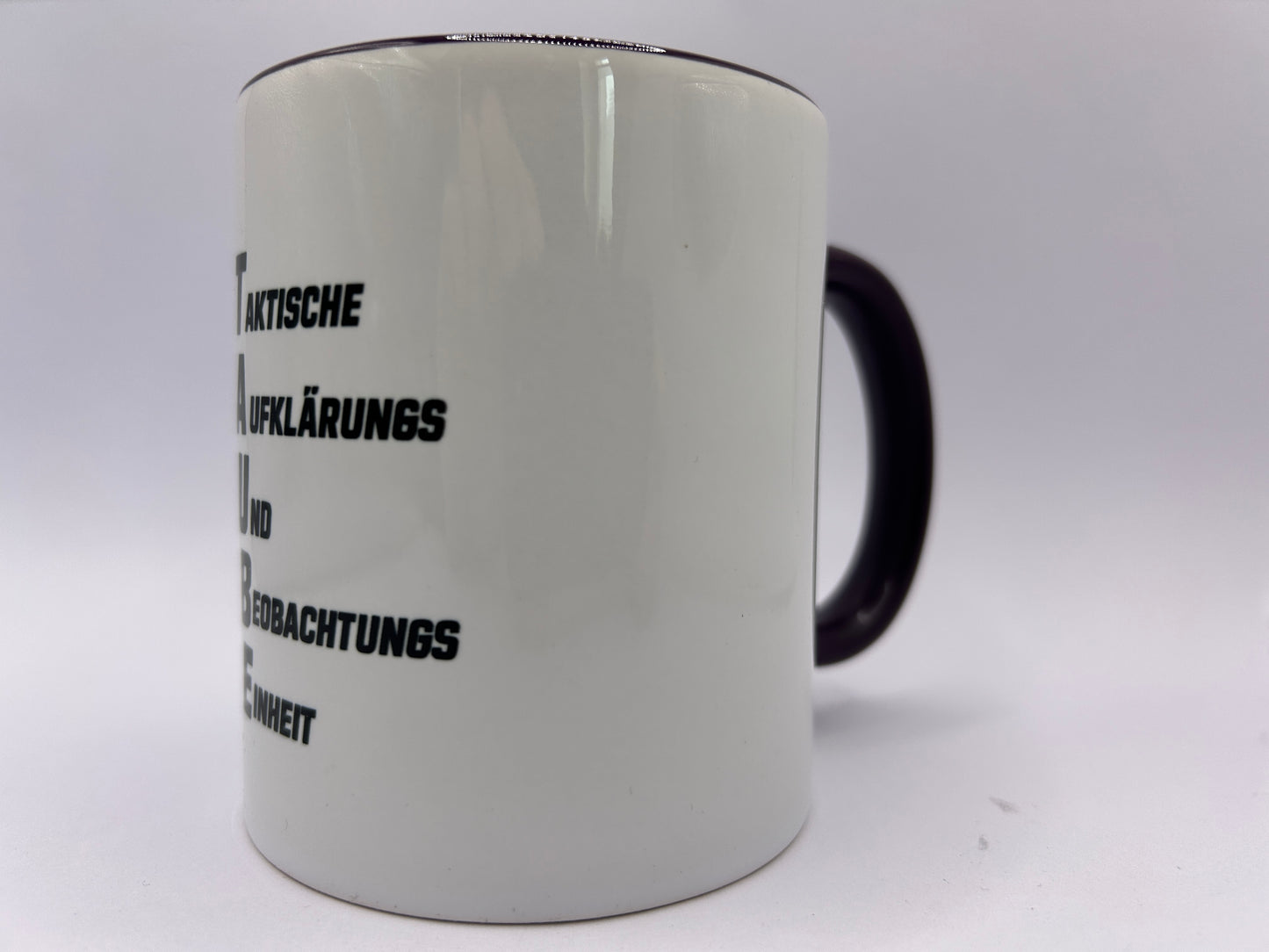 Seitenansicht einer weißen Keramiktasse mit TAUBE-Motiv und schwarzem Henkel. Die humorvolle Militärsatire zeigt eine ausgerüstete Taube als taktische Aufklärungs- und Beobachtungseinheit.